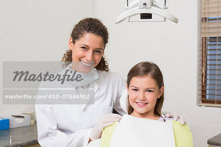 Little girl smiling at camera with her pediatric dentist at the dental clinic