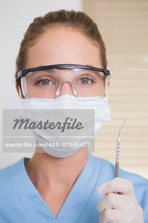 Dentist in surgical mask holding dental explorer at the dental clinic