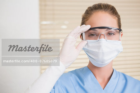 Dentist in surgical mask and protective glasses looking at camera at the dental clinic