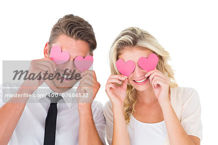Attractive young couple holding pink hearts over eyes on white background