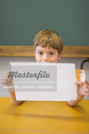 Cute pupil smiling at camera in classroom showing page at the elementary school