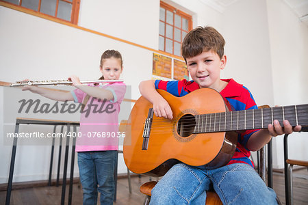 Cute pupils playing flute and guitar in classroom at the elementary school