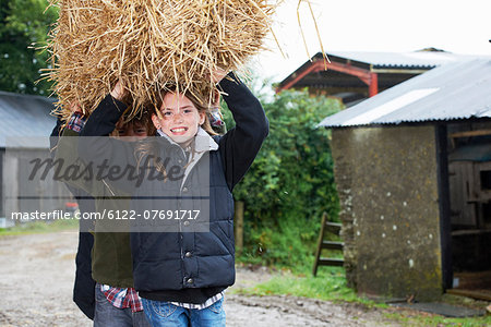 Children carrying straw bale on farm