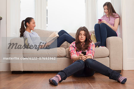 teenage girls sitting on sofa reading , checking messages