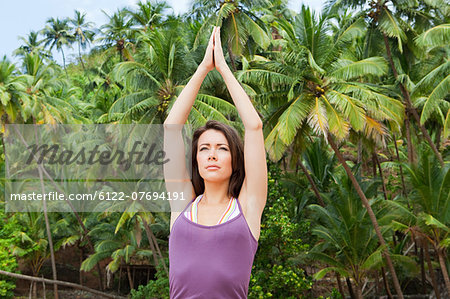 Woman practicing yoga by palm trees