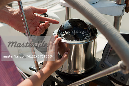 Father and son on board yacht, father pointing to speedometer