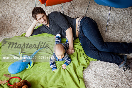 Father playing with baby son in living room