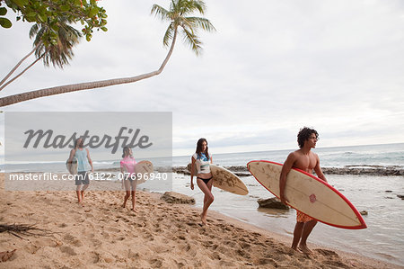 Four young friends carrying surfboards on beach