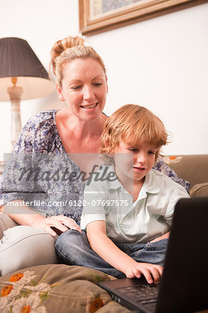 Young boy using laptop with mother looking on encouragingly