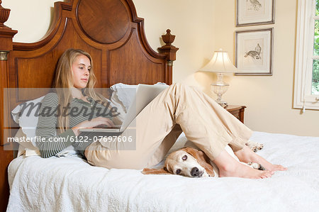 Young woman relaxing on bed with laptop