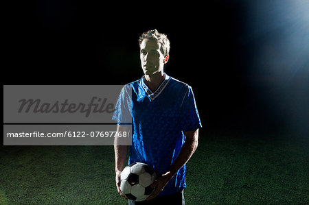 Young man holding soccer ball on pitch