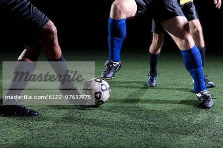 Soccer players tackling on pitch, low section