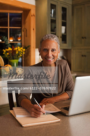 Mature woman using laptop and wearing ear phones, portrait