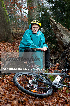 Young man sitting with bicycle in forest