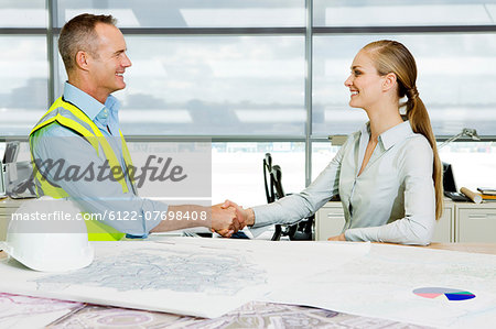 Engineer shaking hands with architect at desk of blueprints in office