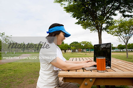 Woman using laptop on picnic bench in the park
