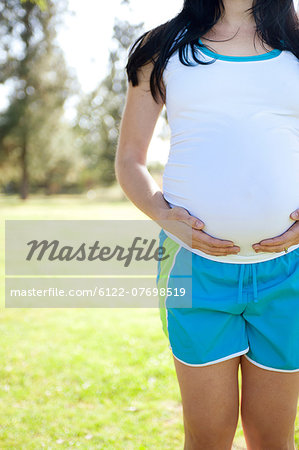 Pregnant young woman touching stomach, front view