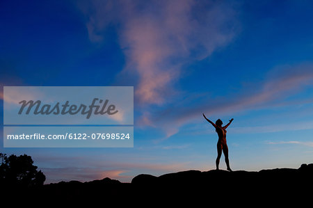Young woman standing in desert with arms open, silhouette