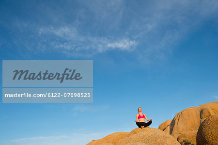 Young woman sitting on desert rocks meditating