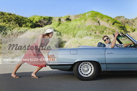 Woman pushing car as boyfriend steers