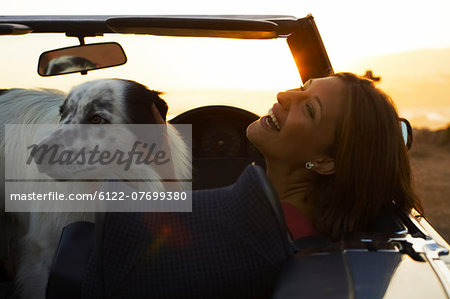 Woman laughing with dog in convertible