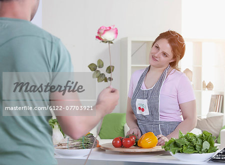 Man giving rose to cooking girlfriend