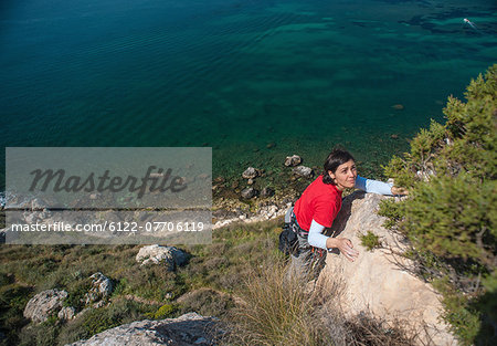 Woman climbing rocky coastal cliff