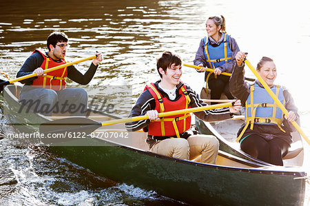 Friends rowing canoes on still lake