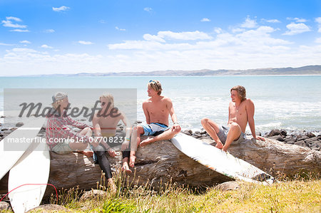 Four young male surfer friends chatting on beach rocks