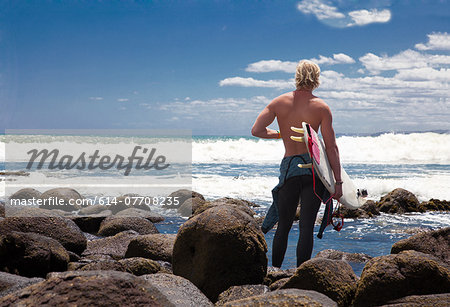 Young adult male surfer watching sea from beach rocks