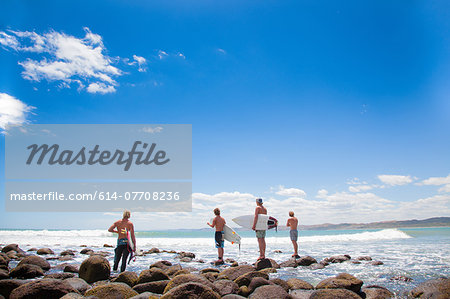 Four young male surfer friends watching sea