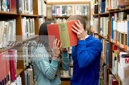 Young couple hiding behind book