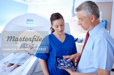 Girl in CT scanner, doctor and radiographer looking at scan on digital tablet