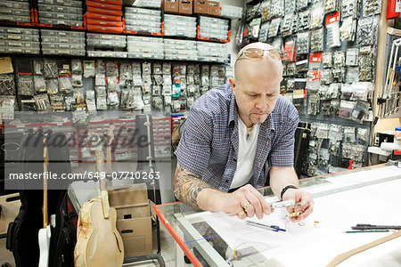 Guitar maker measuring up blueprint design in workshop