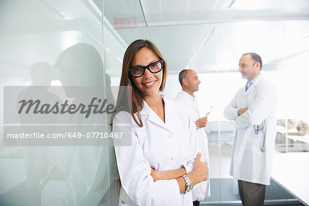 Female doctor by reflective wall, colleagues in background