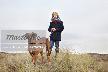 Boy walking his dog in sand dunes at coast