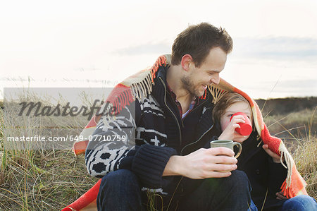 Smiling mid adult man and son wrapped in blanket on sand dunes