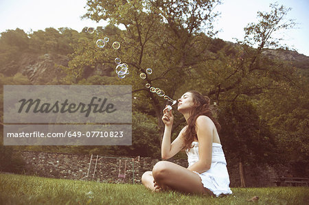 Young woman sitting cross legged in field blowing bubbles