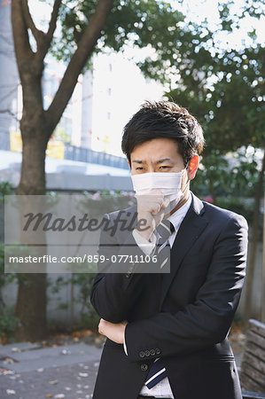 Sick Japanese young businessman in a suit at the park