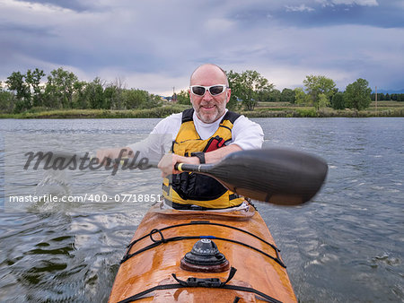 a bow view of a senior male paddling a home-built wooden sea kayak on a lake in Colorado, focus on face with arms and paddle in a motion blur