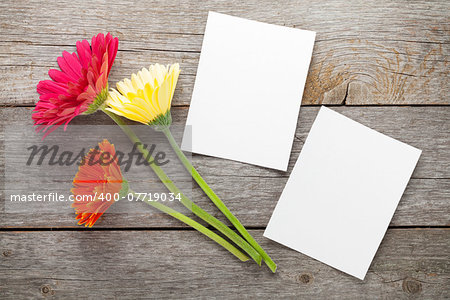 Three colorful gerbera flowers and photo frame on wooden table