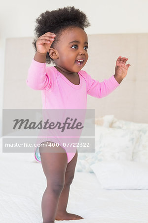 Baby girl in pink babygro standing on bed at home in the bedroom