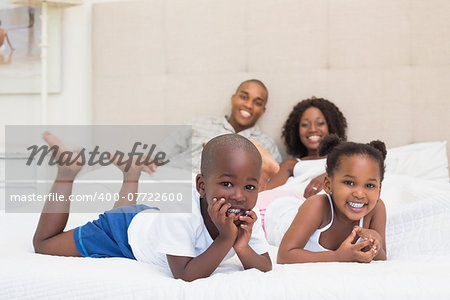 Happy family smiling at camera together on bed at home in the bedroom