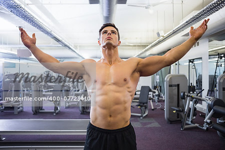 Shirtless bodybuilder with arms raised standing in gym