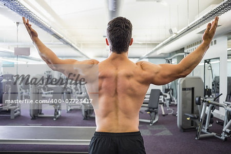 Rear view of a shirtless muscular man with arms raised in gym