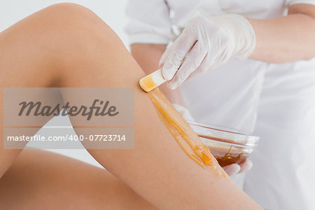 Mid section of therapist waxing woman's leg at spa center