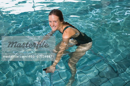 Fit brunette using underwater exercise bike in swimming pool at the leisure centre