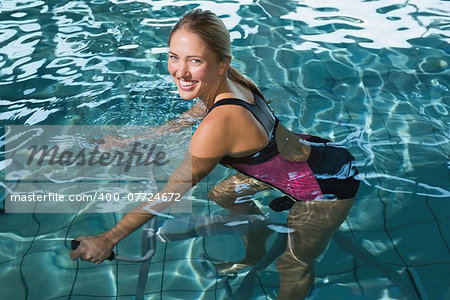 Fit happy blonde using underwater exercise bike in swimming pool at the leisure centre