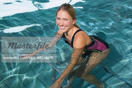 Fit happy blonde using underwater exercise bike in swimming pool at the leisure centre