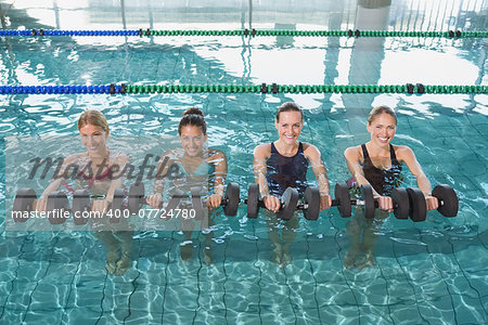 Smiling female fitness class doing aqua aerobics with foam dumbbells in swimming pool at the leisure centre